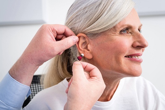 Ältere Frau bekommt ein modernes Hörgerät eingesetzt und lächelt zufrieden.